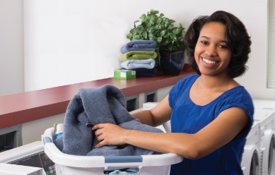 Woman in blue blouse taking a towel out of her laundry basket and smiling at the camera