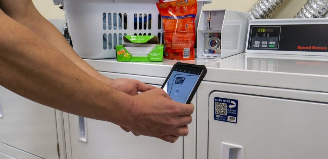 Person using their phone to scan a laundry machine's QR code