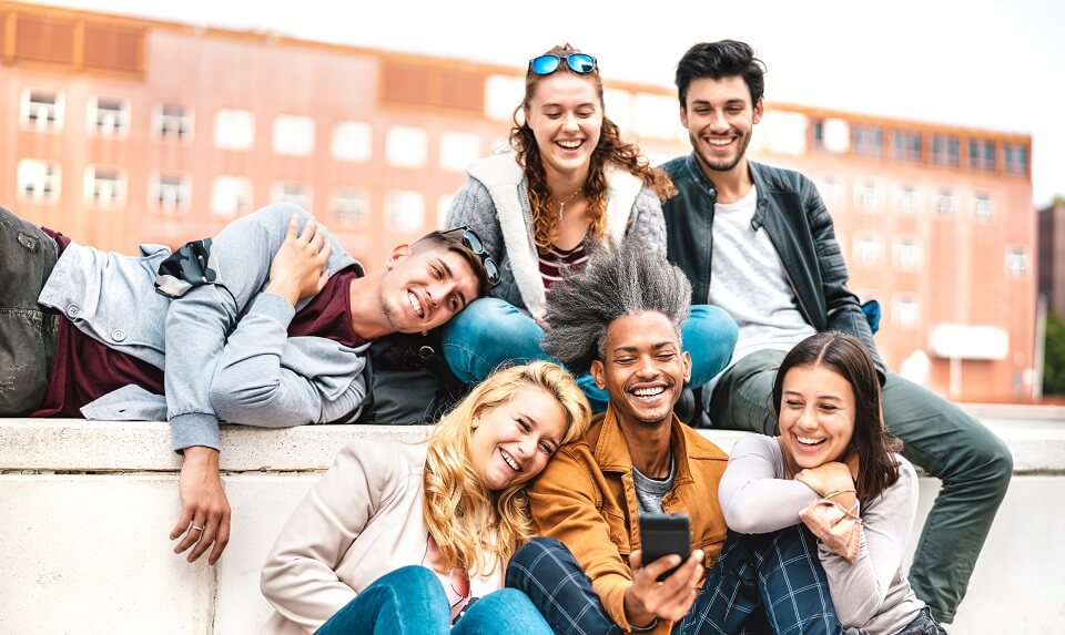 Group of 6 college students looking at a phone and laughing