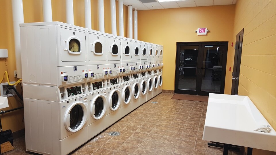 Empty community laundry room with a line of washers with dryers stacked on top