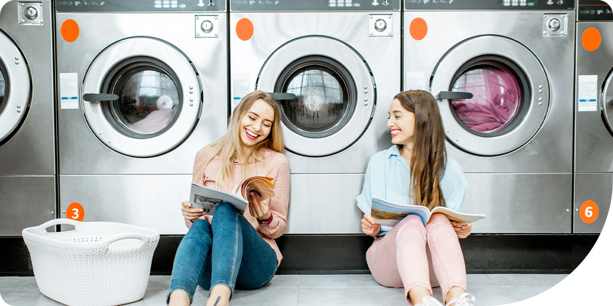 Women sitting in front of multi-housing laundry equipment and reading magazines